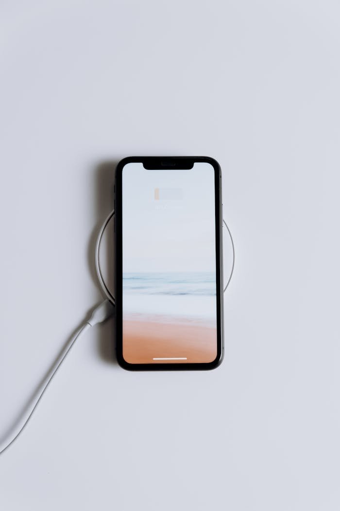 Minimalist smartphone on a wireless charger with a serene beach wallpaper.